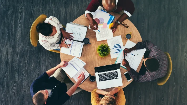 Above, office and people in meeting with graphs for teamwork, collaboration and brainstorming. Business, employees and strategy with laptop or paperwork and unity with statistics, report and strategy.